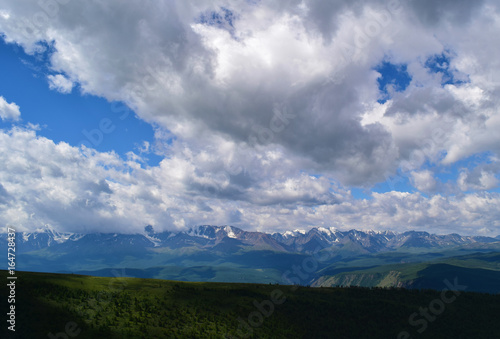 View of snow peaks of North-Chuyski ridge, green hills and blue sky with clouds in Altai mountains. Altay Region, Siberia, Russia.