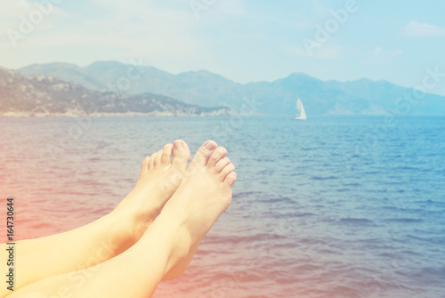 Female feet on a beach against the sea in a summer sunny day, close up, toned. Vacation at the sea