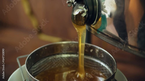 Closeup of honey flowing off harvesting beekeper equipment in apiary photo