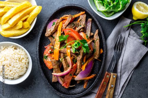 Peruvian dish Lomo saltado - beef tenderloin with purple onion, yellow chili, tomatoes served on black plate, slate background photo