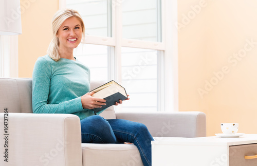 Happy young woman reading a book on her couch at home