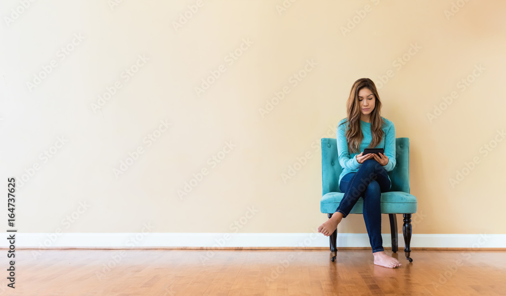 Young latina woman reading with an e-reader in a chair in a large interior room Young latina woman reading with an e-reader in a chair in a large interior room