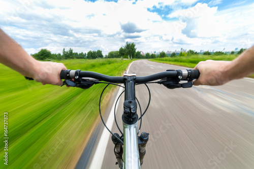 Rider driving bicycle on an asphalt road. Two hand on bike handlebar. Motion blurred background