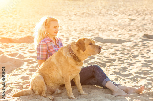 Young woman with her dog at the beach. Sun flare