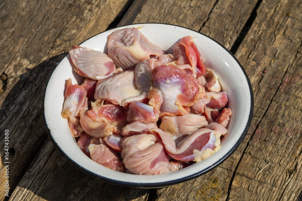 Raw chicken gizzards in metal enamelled bowl on rustic wooden table Raw chicken gizzards in metal enamelled bowl on rustic wooden table