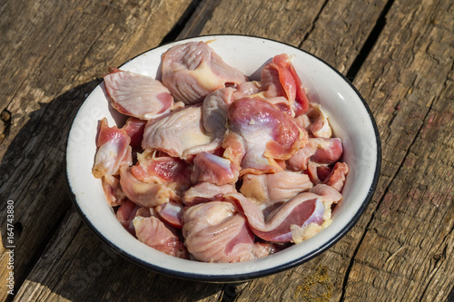 Raw chicken gizzards in metal enamelled bowl on rustic wooden table