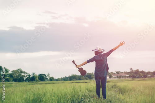 Woman holding ukulele and raise two arms embrace summer sky with puffy clouds,