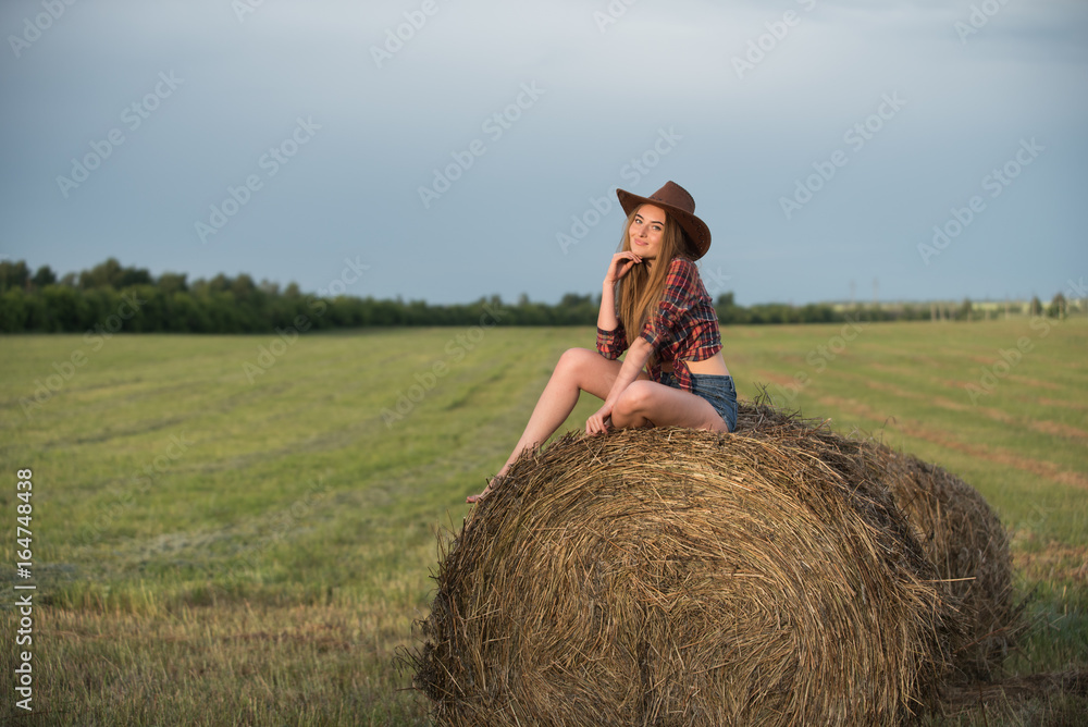 Young woman in shorts and cowboy hat sitting on a haymow Young woman in shorts and cowboy hat sitting on a haymow