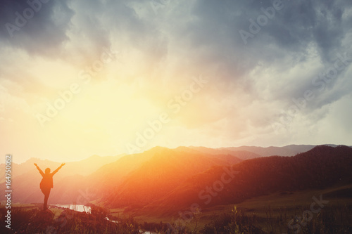 Girl tourist traveler with a backpack standing on cliff of mountain and looking sunset, against backdrop of mountains. Concept active recreation in mountains. Space for text
