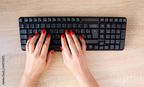 Female hands with red nails on a computer keyboard.