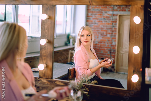 Portrait of a beautiful blonde woman applying makeup near a mirror