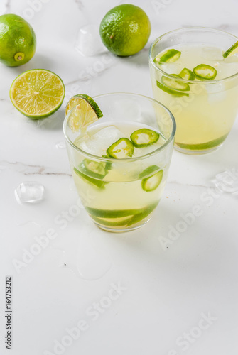 Mexican traditional refreshing drink Fresh Lime and Jalapeno Margarita with tequila, hot pepper and lime (lemon). On a white marble kitchen table. Copy space