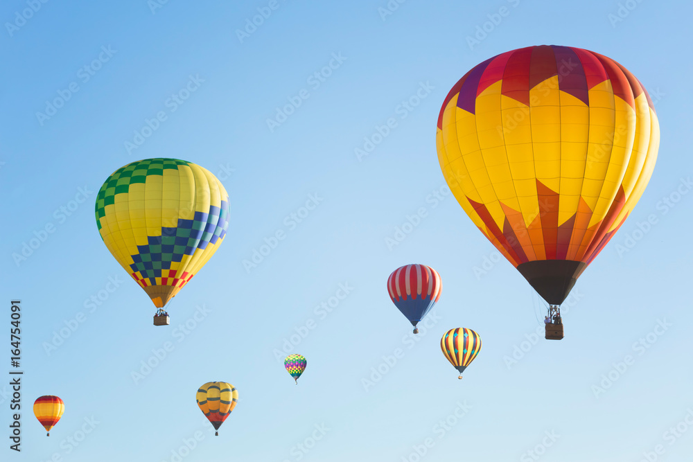 Multi colored hot air balloons in bright morning sky, group of balloons in sunny blue sky photographed from side 