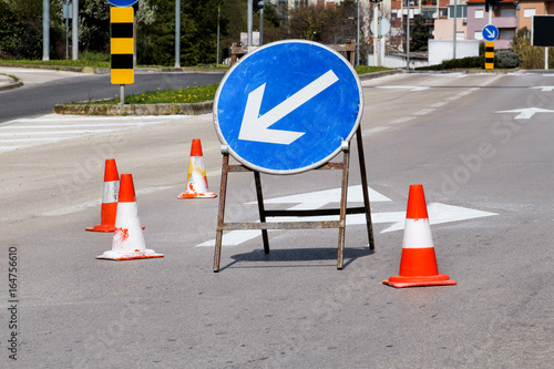 Work on the road. Street signs and road marking. Traffic signs for signaling. Road maintenance, under construction sign and traffic cones on road. Road block with white arrow showing alternate way.