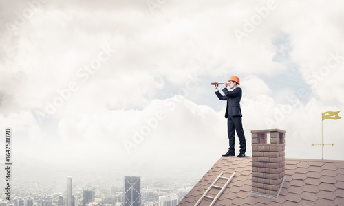 Engineer man standing on roof and looking in spyglass. Mixed med