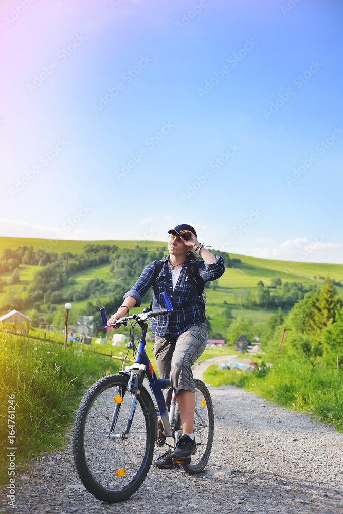 Young woman is traveling with a bicycle in the summer mountains