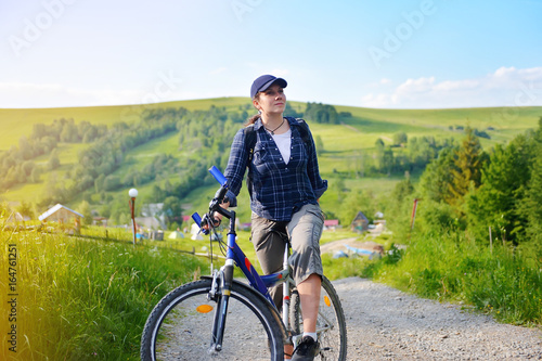 Fototapeta Naklejka Na Ścianę i Meble -  Young woman is traveling with a bicycle in the summer mountains