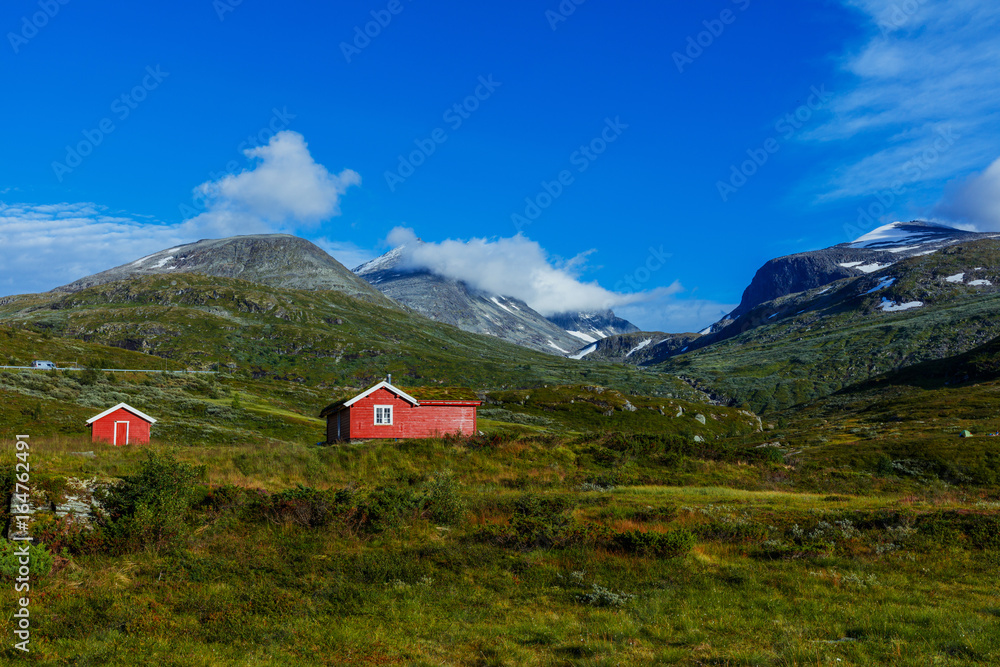 Wooden cottage in the valley. Stone snowy mountains. Norway.