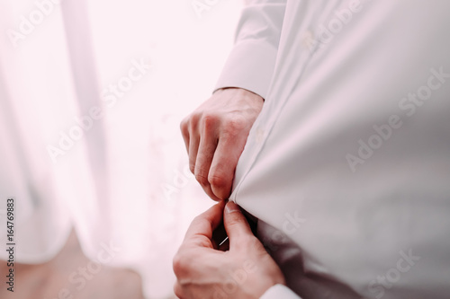 Man gets ready for work by buttoning up his business shirt. Groom s morning preparation before wedding