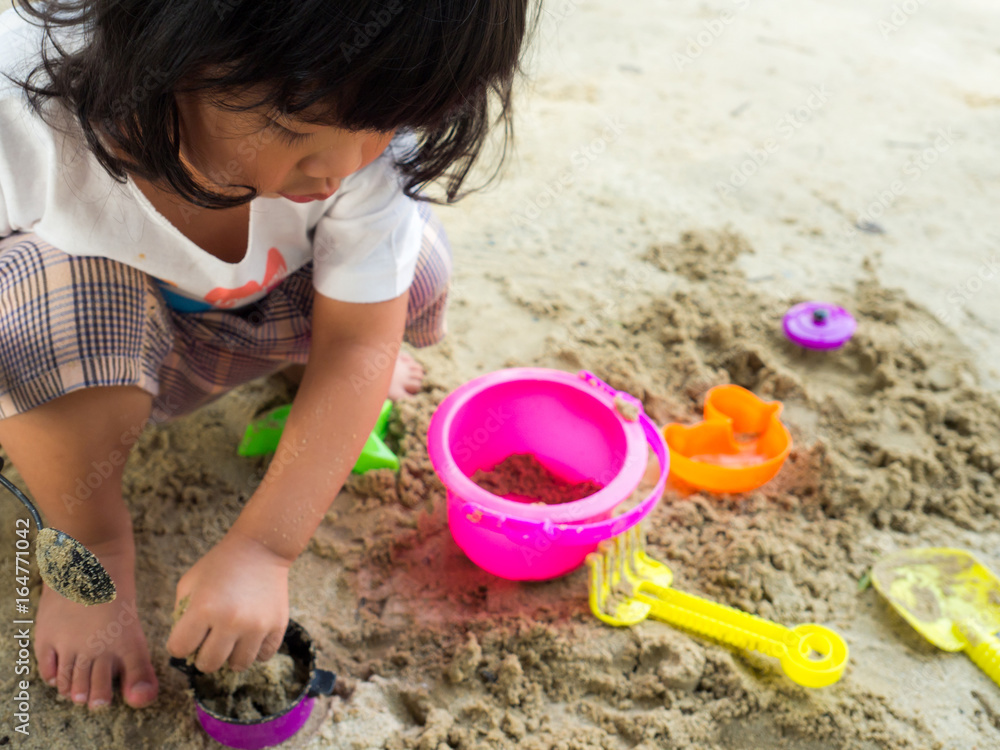 Little Asia girl sitting in the sandbox and playing whit toy shovel bucket and she was scooping in toy shovel bucket. Playing is a learning development and build muscle for children. Little Asia girl sitting in the sandbox and playing whit toy shovel bucket and she was scooping in toy shovel bucket. Playing is a learning development and build muscle for children.