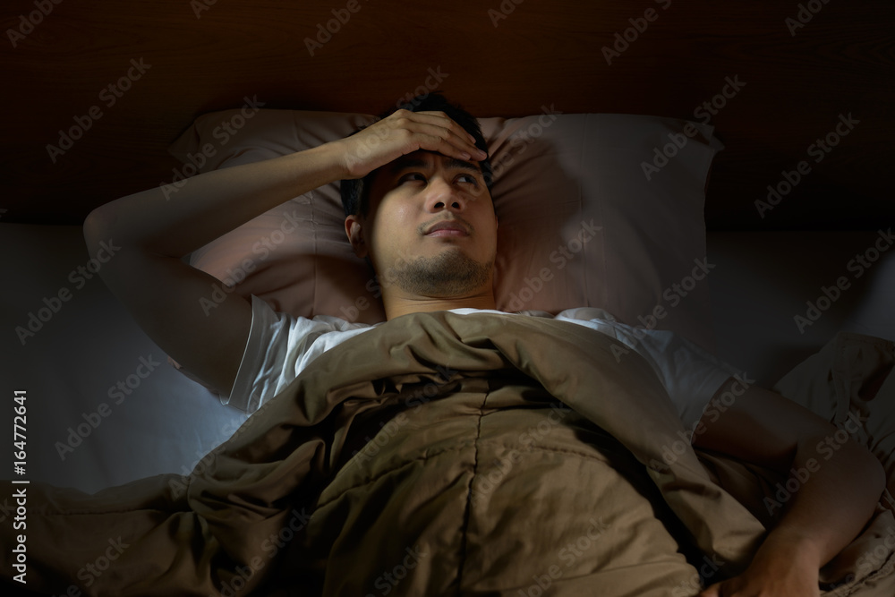 Depressed man suffering from insomnia lying in bed Depressed man suffering from insomnia lying in bed