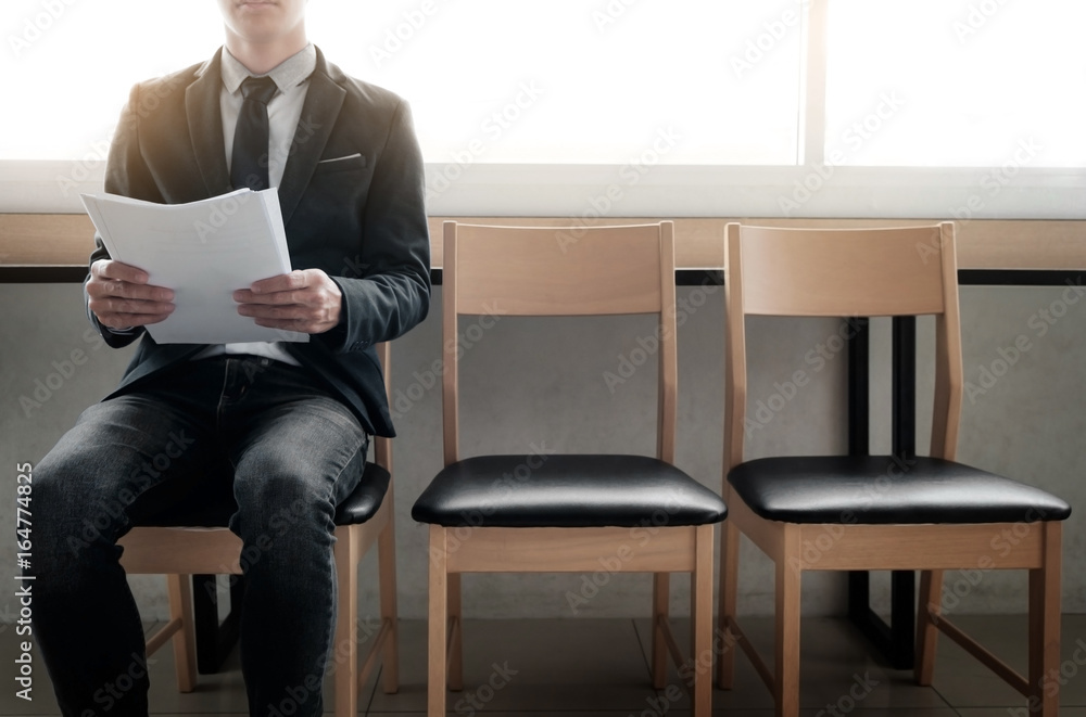 Confident young businessman holding paper while sitting on a row of chairs, waiting for interview. Confident young businessman holding paper while sitting on a row of chairs, waiting for interview.