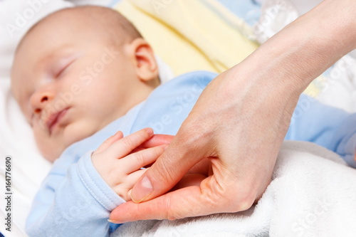 Mother holding hand of sleeping newborn baby