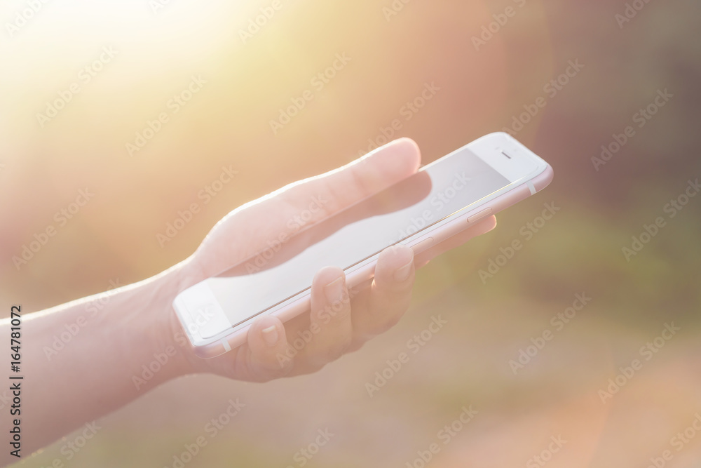 Hand of woman holding or using smartphone on green blur and sunlight effect Hand of woman holding or using smartphone on green blur and sunlight effect