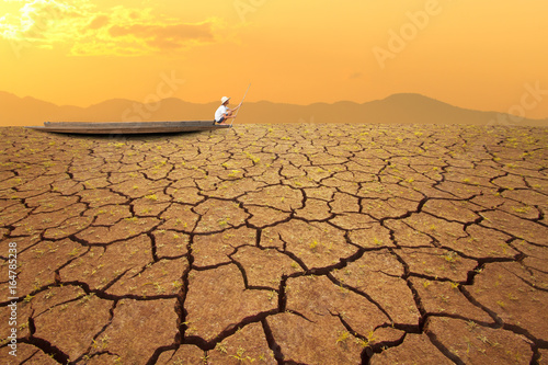 Climate change, Young man Paddle wooden Boat on dry and cracked earth with sunset sky background