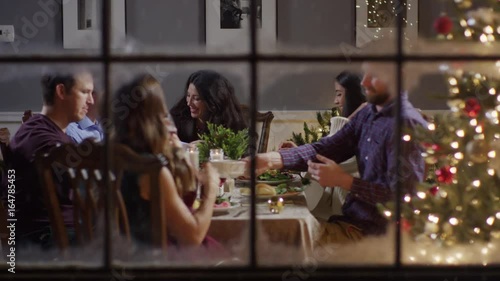 Medium zoom out shot of family eating meal on Christmas behind window / Cedar Hills, Utah, United States