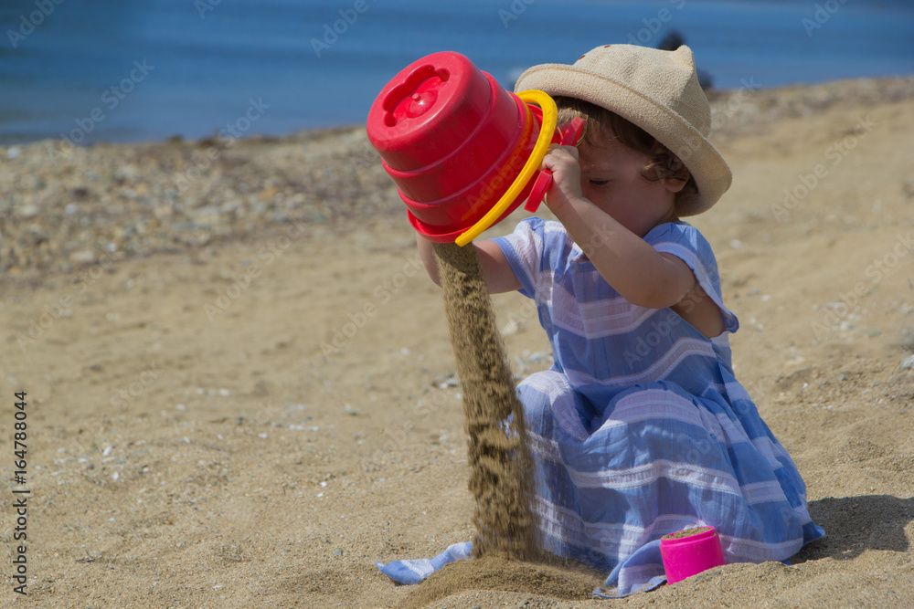 Little girl in a hat playing with sand on the beach Little girl in a hat playing with sand on the beach