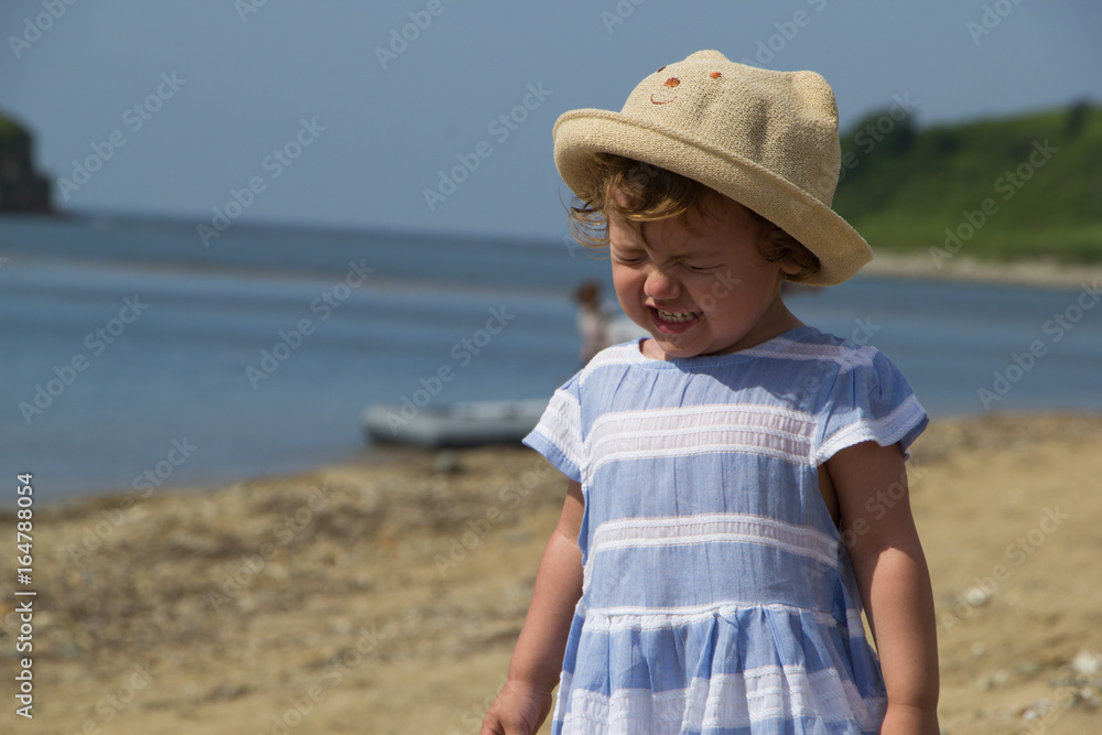 Little girl in a hat crying on the beach