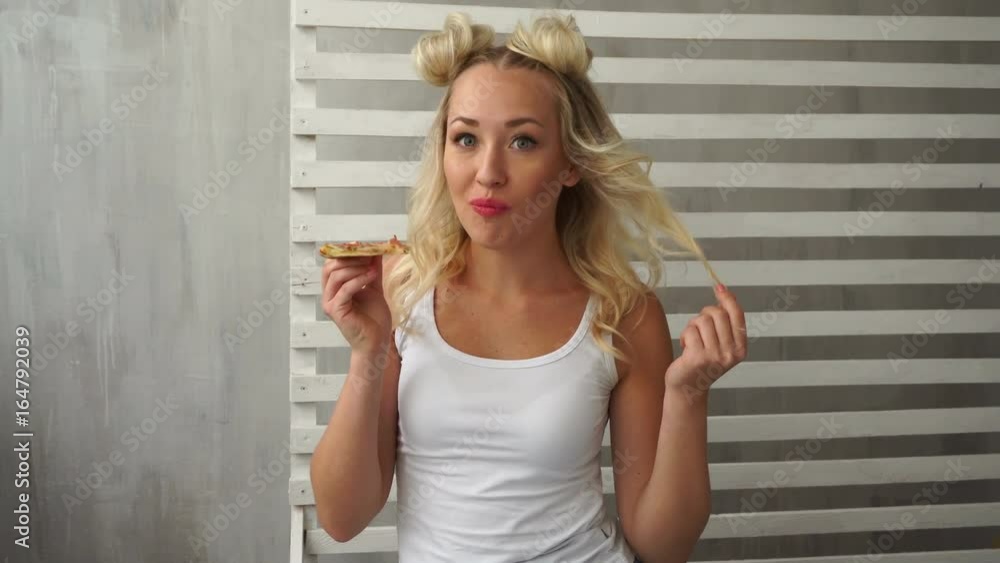 Young attractive girl eats pizza with delight. A hipster girl with a fashionable haircut is dressed in a white T-shirt. Close-up Young attractive girl eats pizza with delight. A hipster girl with a fashionable haircut is dressed in a white T-shirt. Close-up