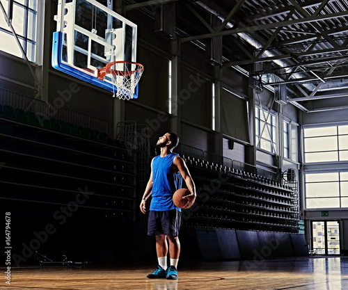 Basketball player holds a ball over the hoop in a game hall.