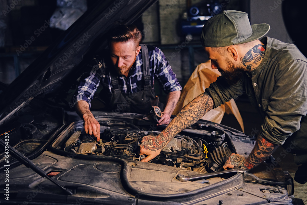 Two mechanics fixing car's engine in a garage.