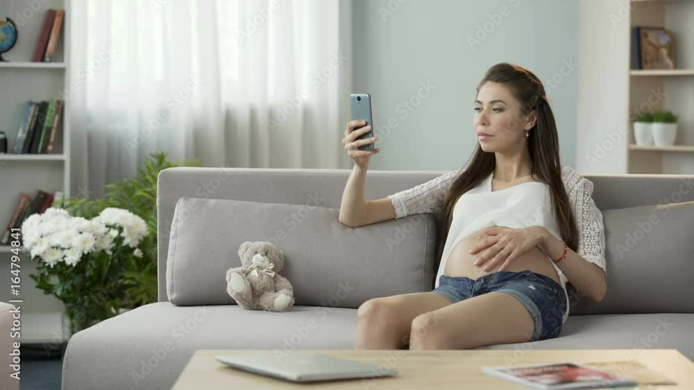Female pregnant with child sitting on sofa and using mobile phone, online blog Female pregnant with child sitting on sofa and using mobile phone, online blog