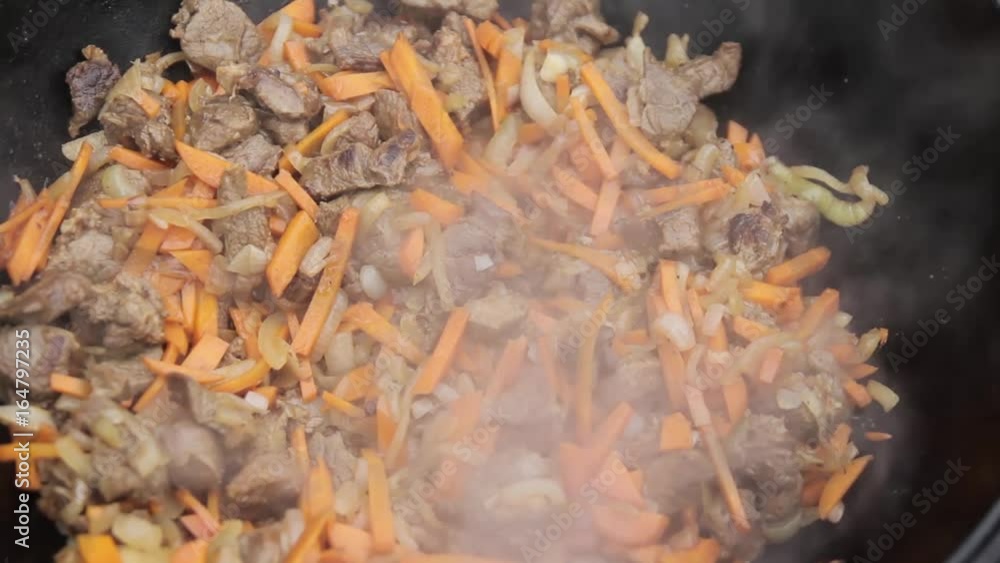 Cooking of pilaff with lamb, carrots and spices onions in a cauldron on a wood stove Cooking of pilaff with lamb, carrots and spices onions in a cauldron on a wood stove