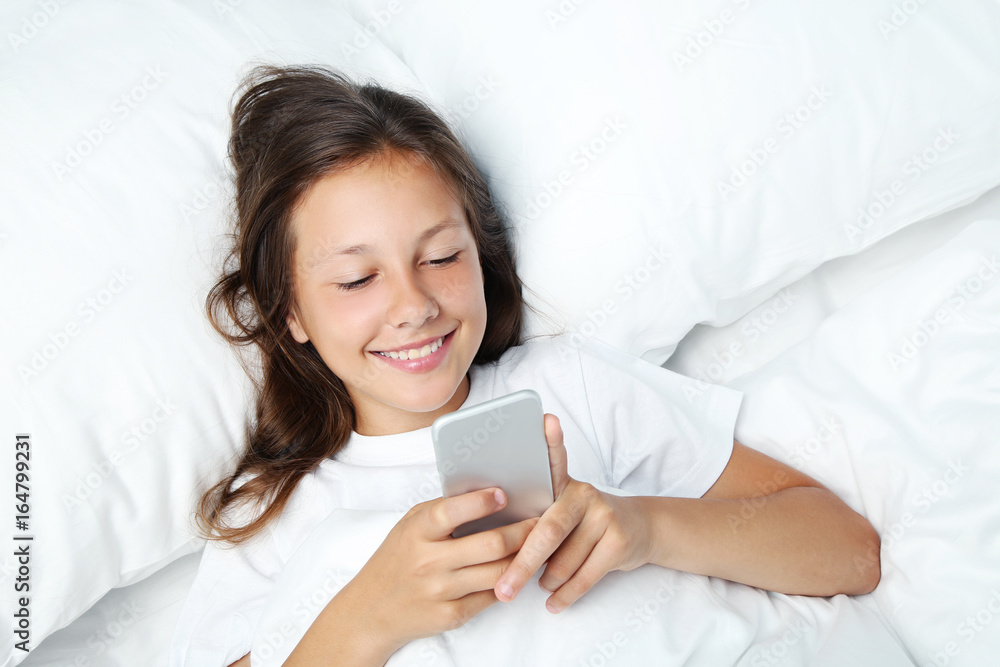 Beautiful girl with smartphone lying in white bed Beautiful girl with smartphone lying in white bed