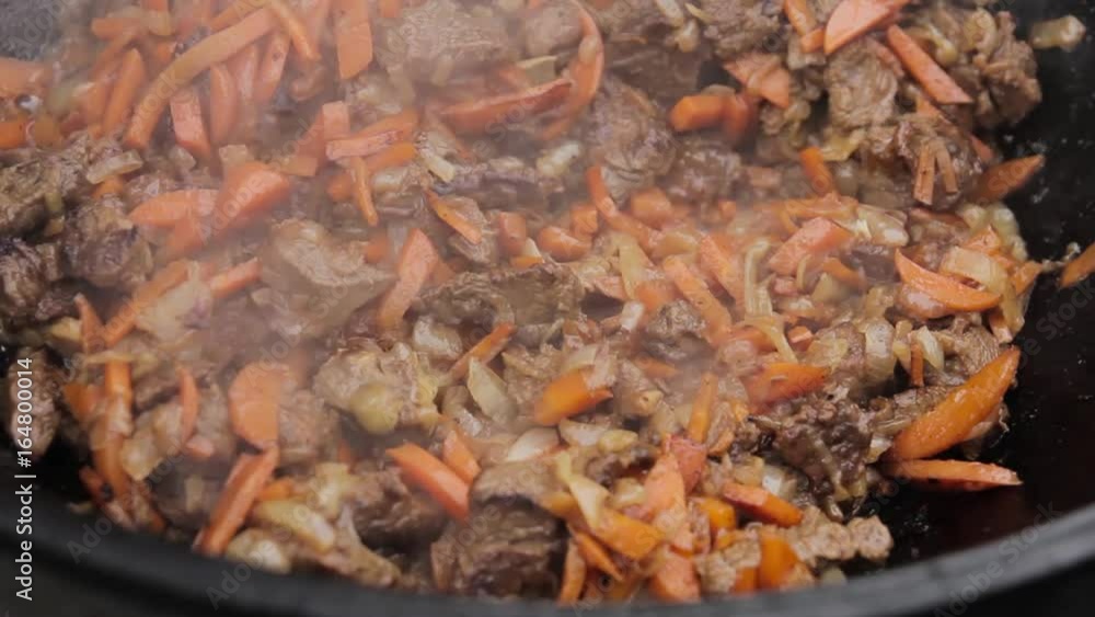 Cooking of pilaff with lamb, carrots and spices onions in a cauldron on a wood stove Cooking of pilaff with lamb, carrots and spices onions in a cauldron on a wood stove