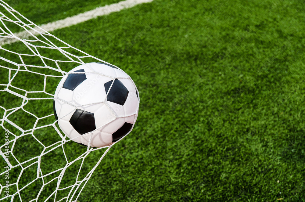 Naklejka premium Soccer football in Goal net with green grass field.