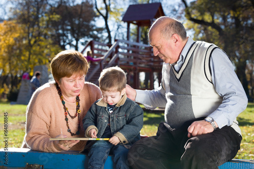 grandparents with grandson reading book in a park in autumn © dobok