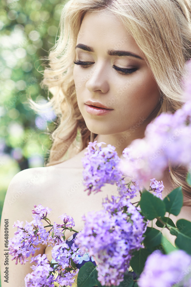 Outdoor fashion beautiful young woman surrounded by lilac flowers summer. Spring blossom lilac bush. Portrait of a girl blondes Outdoor fashion beautiful young woman surrounded by lilac flowers summer. Spring blossom lilac bush. Portrait of a girl blondes