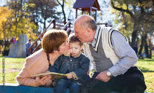 grandparents with grandson reading book in a park in autumn © dobok