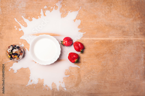 plate with spilled milk, strawberries and nuts on wooden background;