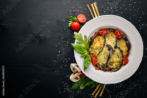 Baked eggplant with parmesan cheese. On a black wooden surface. Free space for your text. Top view.