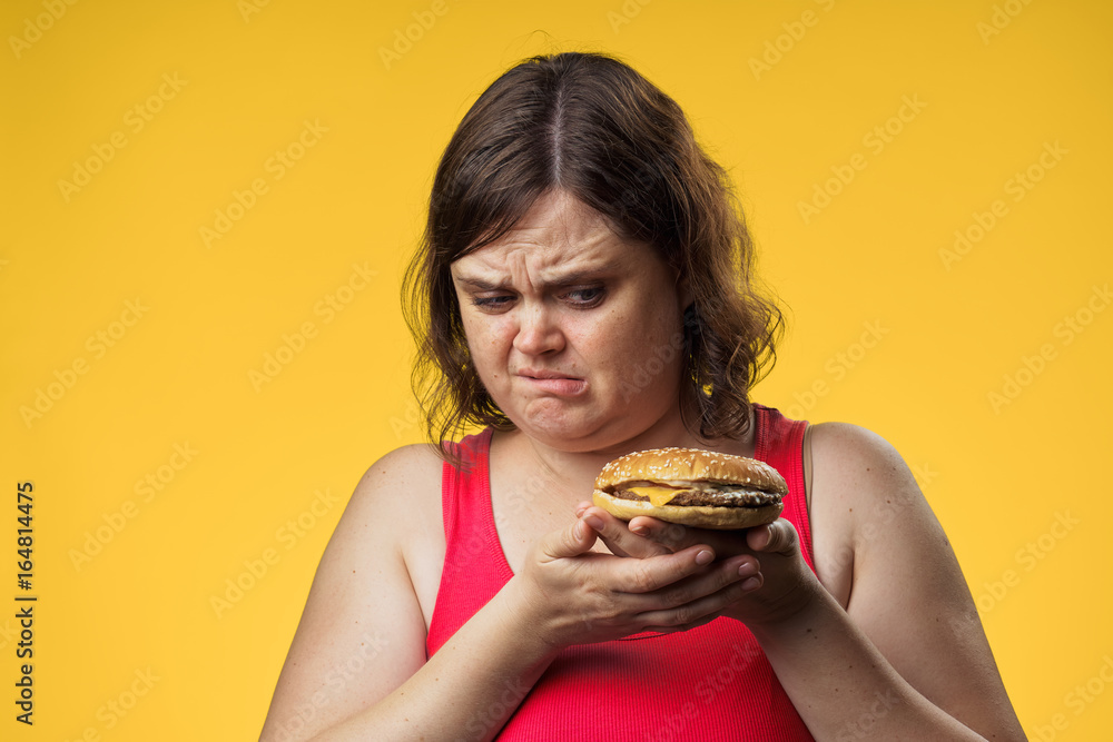 Fat woman on a yellow background holds a hamburger, fast food Fat woman on a yellow background holds a hamburger, fast food