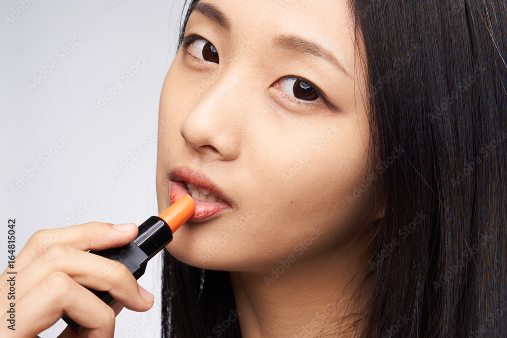 Beautiful young woman on a light background paints lips, asian Beautiful young woman on a light background paints lips, asian