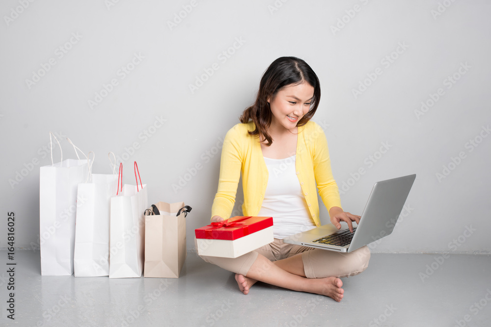 Young asian woman sitting besides row of shopping bags holding red gift box Young asian woman sitting besides row of shopping bags holding red gift box