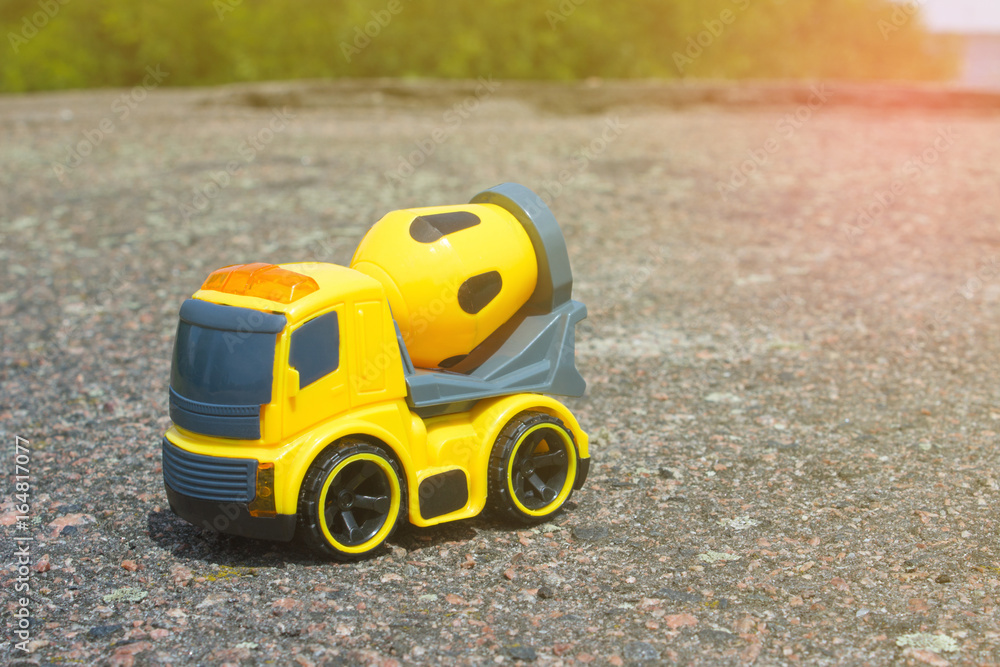 Toy car mixer on the dark asphalt against the backdrop of bushes and trees Toy car mixer on the dark asphalt against the backdrop of bushes and trees
