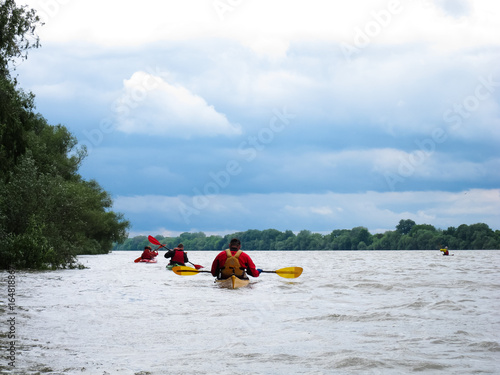 Group of people (friends) kayaking in wild river and lake on biosphere reserve in spring on cloudy spring day © watcherfox